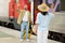 Smiling young caucasian woman meets boyfriend with suitcase from trip, waving hand at train station