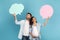 Smiling young european guy and arab pregnant lady hold abstract clouds, bubbles with empty space