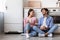 Smiling young european lady and guy with cups drink coffee in morning sitting on floor, communication