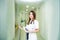 Smiling young female medical professional, doctor with stethoscope and smart phone looking at camera and opening the door to her