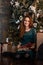 Smiling young girl in green dress with presents and gift boxes under the Christmas tree