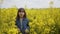 Smiling young girl in jeans jacket walking through blooming fresh yellow canola field