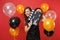 Smiling young girl in little black dress hiding behind classic black film making clapperboard on bright red background