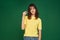 Smiling young girl showing little size gesture with fingers on green studio background. Small prices, sale, big discount