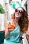 A smiling young girl in sunglasses sits in a summer cafe on the street and drinks a cool alcoholic cocktail. Rest, enjoyment,