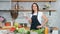 Smiling young housewife in apron trying cucumber dancing cooking healthy food at cozy kitchen