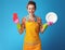 Smiling young housewife with sponge and plate on blue