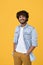 Smiling young indian guy standing isolated on yellow background. Vertical