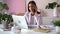 Smiling young Indian mixed-race business woman professional talking on phone using laptop sit at office desk
