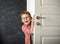 Smiling young kid boy peeking out of door. School kid come back from school. Happy child in glasses. Hand on handle