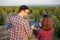 Smiling young male and female agronomists and farmers inspecting young fruit orchard, using tablet