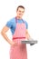 Smiling young man in an apron holding a baking tray