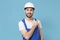 Smiling young man in coveralls protective helmet hardhat isolated on blue wall background. Instruments accessories for