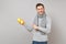 Smiling young man in gray sweater, scarf pointing index finger on lemons in hand on grey background. Healthy