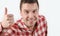 Smiling young man in hipster shirt showing thumb up and standing against white background