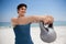 Smiling young man holding kettlebell at beach
