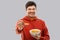 Smiling young man in red hoodie eating cereals