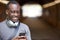 Smiling Young Man In Urban Setting Checks Social Media And Messages On Mobile Phone Whilst Wearing Wireless Headphones