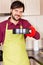 Smiling young man wearing cooking mitten and apron holding a baking tray