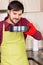 Smiling young man wearing cooking mitten and apron holding a baking tray