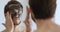 Smiling young metrosexual man applying facial mask looking in mirror