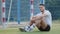 Smiling young Middle Eastern Indian guy footballer sitting on soccer field against goal, happy with results of game