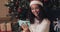 Smiling young mulatto girl in santa\'s hat sitting under Christmas Tree and Having a Video Call using her Modern Mobile