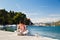 Smiling young pretty woman sitting cross-legged on pier holding mobile phone with fantastic croatian sea coast view in