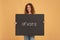 Smiling young redhead curly female holding holding vote sign, poster or banner with inscription