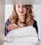 Smiling young woman arranging a pile of towels on a shelf on white bricks background