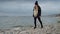 Smiling young woman with a backpack exploring a rocky sea beach in cold, windy weather. Ideal for travel.