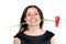 Smiling young woman in black dress holds a gerbera flower in teeth, isolated over white background