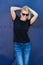 Smiling young woman in black t shirt and sunglasses against blue metal background t shirt mock up