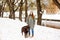 Smiling young woman with brown dog labrador in winter warm outfit walking outdoors in snowy park