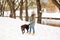 Smiling young woman with brown dog labrador in winter warm outfit walking outdoors in snowy park
