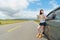 Smiling young woman with car on asphalt roadside