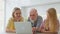 Smiling young woman and daughter show an old father how to use applications on laptop while relaxing at home in living