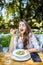 Smiling young woman enjoys fresh vegetable salad at cafe, has lunch after work, keeps to diet, eats only healthy food, being satis