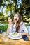 Smiling young woman enjoys fresh vegetable salad at cafe, has lunch after work, keeps to diet, eats only healthy food, being satis