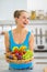 Smiling young woman with fruits plate in kitchen