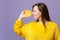 Smiling young woman in fur sweater hold, looking aside on half of fresh ripe orange fruit isolated on violet pastel wall