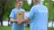 Smiling young woman giving donation box to senior volunteer, assistance project