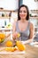 Smiling young woman in a gray T-shirt squeezes a fresh orange on fruit juice. Healthy eating concept. In the interior of the