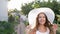 Smiling young woman into hat with wide brim attracted to herself and runs ahead