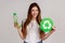 Smiling young woman holding plastic bottle and green sign, waste sorting and sustainability.