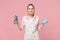 Smiling young woman housewife in apron hold atomizer spray with washing cleanser, cleaning rag while doing housework