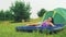 A smiling young woman lies on an inflatable mattress next to a tent in a forest glade.