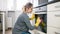 Smiling young woman polishing oven glass door on kitchen