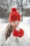 Smiling young woman in red knitted mittens holds cup of hot drink outdoors. Warm drinks in winter