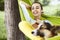 Smiling young woman resting in green hammock with funny dog Welsh Corgi in a park outdoors. Beautiful happy female in